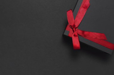 Siyah hediye kutusu koyu arka plan en iyi görünüm düz kırmızı kurdele ile yatıyordu. Tatil kavramı, Doğum günü hediyesi, babalar günü, Sevgililer günü, yeni yıl veya Noel Xmas Tebrikler arka plan sunar