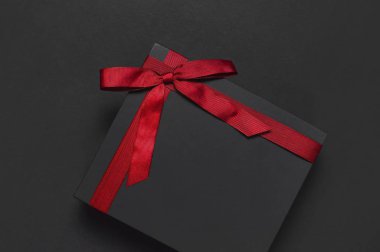 Siyah hediye kutusu koyu arka plan en iyi görünüm düz kırmızı kurdele ile yatıyordu. Tatil kavramı, Doğum günü hediyesi, babalar günü, Sevgililer günü, yeni yıl veya Noel Xmas Tebrikler arka plan sunar