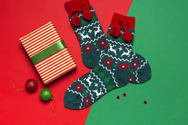 Woolen socks with a Christmas New Year ornament, gift box, balls, glitter confetti on red green background top view flat lay. Holiday concept, presents Xmas. Congratulations background space for text