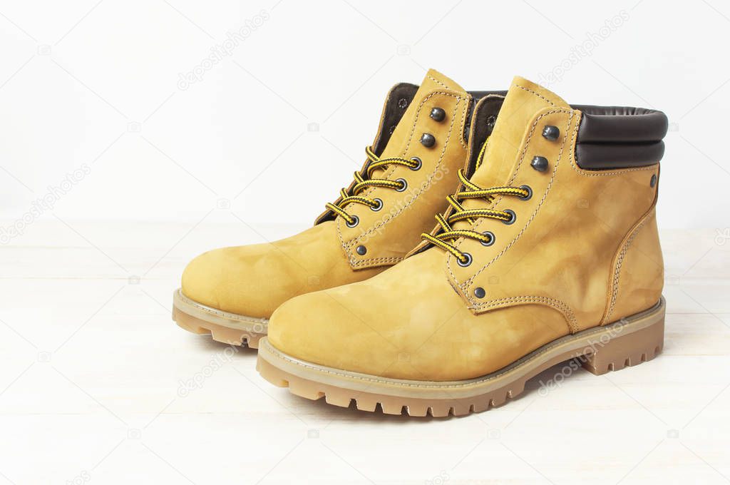 Yellow men's work boots from natural nubuck leather on wooden white background. Trendy casual shoes, youth style. Concept of advertising autumn winter shoes, sale, shop