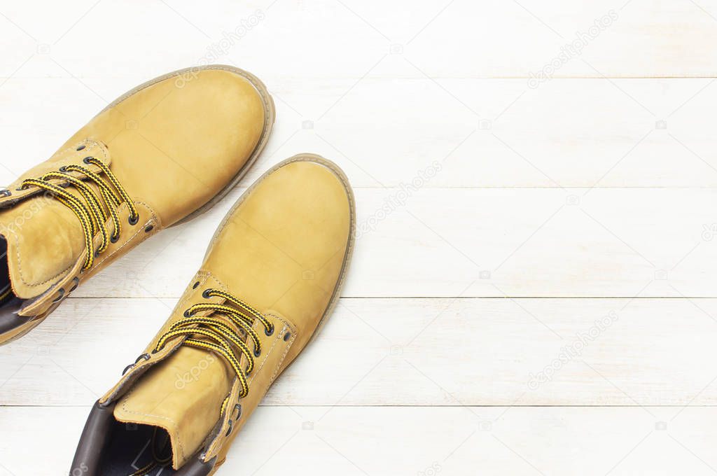 Yellow men's work boots from natural nubuck leather on wooden white background top view flat lay with copy space. Trendy casual shoes, youth style Concept of advertising autumn winter shoes sale shop