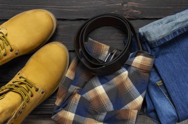 Erkek giyim, sarı iş botları doğal nubuk deri, mavi jeans, kareli gömlek ve düz yatıyordu kopya alanı görüntülemek kahverengi kemer koyu ahşap arka plan üstüne. Modaya uygun rahat ayakkabı, gençlik stili