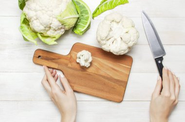 Karnabahar ile kesme tahtası üzerinde bıçak, mutfak havlusu rustik beyaz ahşap zemin üstüne kesmek eller görüntülemek düz yatıyordu kopya alanı. Yemek, sağlıklı sağlıklı gıda, sebze, diyet kavramı