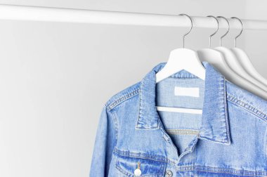 Mavi kot ceket karşı açık gri bir çubuk üzerinde beyaz ahşap askı üzerinde duvar düz yatıyordu kopya alanı. Denim, moda ceket, kadın ya da erkek trend giyim, moda arka plan. Mağaza konsepti, Satılık