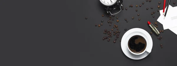 Flat lay cup black coffee, coffee beans, black alarm clock, red lipstick, color pencils, white cards on gray dark background top view copy space. Creative Concept time to work female desktop