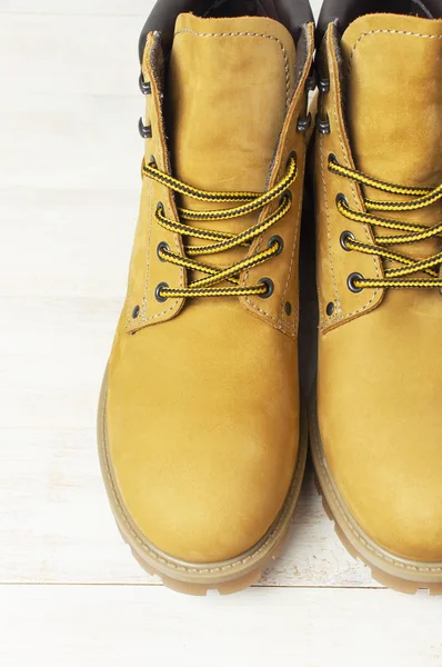 Close-up Yellow men\'s work boots from natural nubuck leather on wooden white background. Trendy casual shoes, youth style. Concept of advertising autumn winter shoes, sale, shop