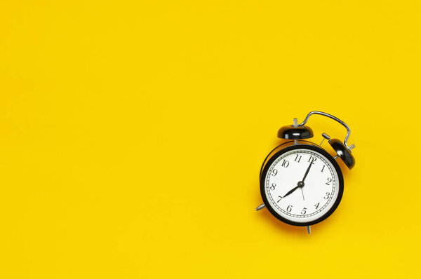 Black retro alarm clock on yellow background top view Flat lay copy space. Minimalistic background, concept of time, deadline, time to work, morning.