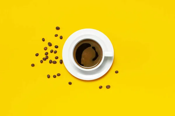 Flat lay cup of black coffee and coffee beans on yellow background top view copy space. Minimalistic food concept, morning breakfast, time to work, hot drink, coffee background.