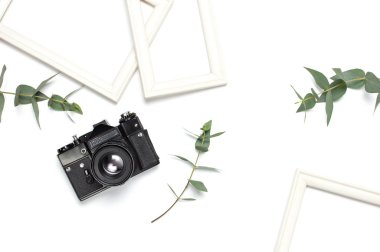 Beyaz fotoğraf çerçevesi, eski retro fotoğraf kamera ve yeşil okaliptüs beyaz zemin üzerine bırakır. Düz yatıyordu üstten görünüm kopya alanı. Şık en az kompozisyon, resim mockup, resim çerçevesi, ev dekorasyon.