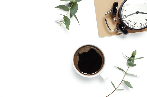 Flat lay cup of black coffee, black alarm clock, notebook, diary, eucalyptus on white background top view copy space. Minimalistic food concept, Feminine desk workspace, time to work coffee background.