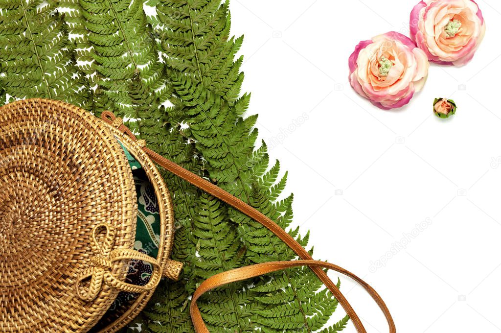 Fashionable handmade natural organic rattan bag and green fern leaves, pink flower isolated on white background. Ladies bag, Stylish rattan bag. Flat lay, top view, copy space. Ecobags from Bali.