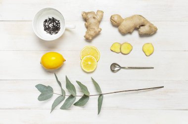 Fresh ginger root, cup tea with brewing inside, lemon, eucalyptus leaves on white wooden background. Flat lay, top view, copy space. Minimalistic style, seasoning, spice, ingredient for tea. clipart
