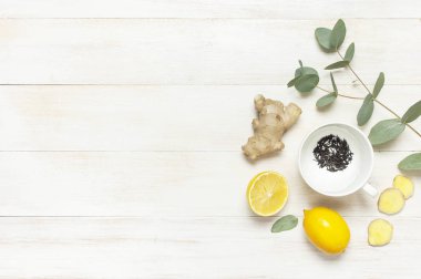 Fresh ginger root, cup tea with brewing inside, lemon, eucalyptus leaves on white wooden background. Flat lay, top view, copy space. Minimalistic style, seasoning, spice, ingredient for tea. clipart