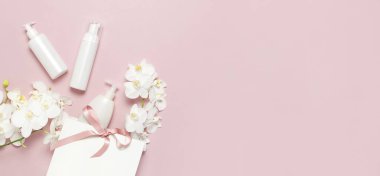 Düz üstten görünüm beyaz kozmetik şişe kapları hediye çanta beyaz Phalaenopsis orkide çiçek pembe bir arka plan üzerinde yatıyordu. Mock-up doğal organik güzellik ürün kavramı minimalizm tarzı marka kozmetik Spa