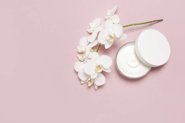 Güzellik Spa kavramı. Krem ve pembe bir arka plan düz beyaz Phalaenopsis orkide çiçekler ile açılan plastik konteyner üstten görünüm yatıyordu. Bitkisel Dermatoloji kozmetik hijyenik krem, organik kozmetik doğal