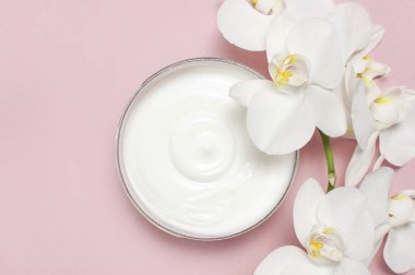 Güzellik Spa kavramı. Krem ve pembe bir arka plan düz beyaz Phalaenopsis orkide çiçekler ile açılan plastik konteyner üstten görünüm yatıyordu. Bitkisel Dermatoloji kozmetik hijyenik krem, organik kozmetik doğal