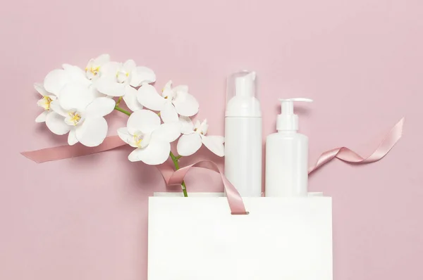 Düz üstten görünüm beyaz kozmetik şişe kapları hediye çanta beyaz Phalaenopsis orkide çiçek pembe bir arka plan üzerinde yatıyordu. Mock-up doğal organik güzellik ürün kavramı minimalizm tarzı marka kozmetik Spa