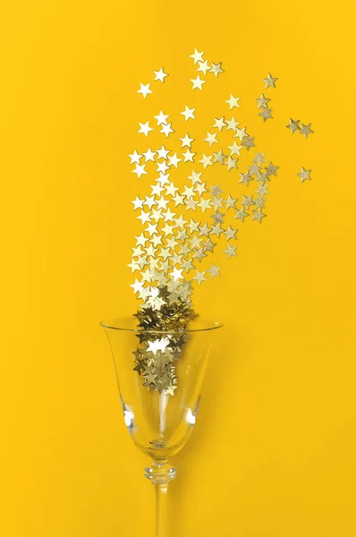 Confiti de oro en forma de estrellas vuelan fuera de copas de champán sobre fondo amarillo Flat lay Vista superior. Composición creativa, concepto de fuegos artificiales, vacaciones, fiesta, cumpleaños, Navidad o año nuevo — Foto de Stock