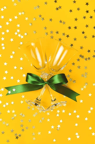 Kieliszki do szampana z zielonej wstążki, złotym konfetti w kształcie gwiazdek na żółtym tle z płaskim leżał widok z góry. Kreatywnych kompozycji, pojęcie fajerwerk holiday party urodziny Boże Narodzenie nowy rok — Zdjęcie stockowe