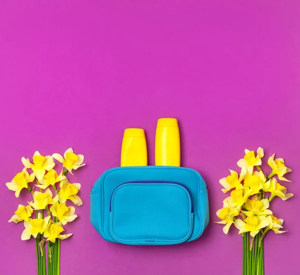 Female cosmetics bag, cosmetic products, sunscreen cream, spray, yellow narcissus daffodil flowers on bright pink fuchsia background top view flat lay. Minimalism cosmetics style Bright summer concept