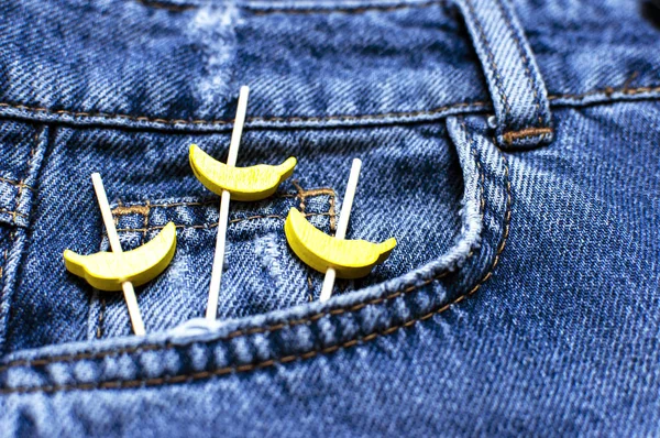 Niebieskie dżinsy i żółte drewniane banany z kieszeni na czarnym tle góry widok płaski lay. Szczegóły ładne niebieskie dżinsy. Dżinsy tekstury lub denim tle. Odzież trend. Moda, koncepcja odzieży. — Zdjęcie stockowe