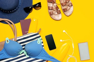 Kadın yaz Giyim Aksesuarları Sarı zemin üzerine. Seyahat tatil deniz kavramı. Şapka takım elbise kot şort deri sandalet güneş gözlüğü güneş deniz çanta pasaport telefon yüzme. Düz yatıyordu Üstten Görünüm