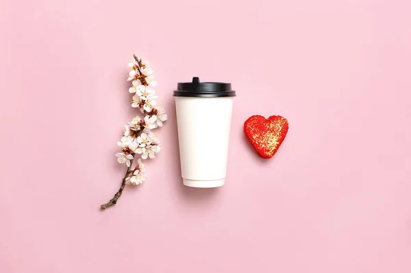 Coffee or tea paper cup, heart-shaped macaroon cakes, spring branches of white flowers on pink background top view flat lay. Take away coffee cup, mockup. Coffee love concept, layout for design