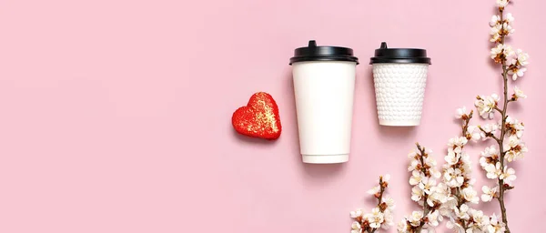 Coffee or tea paper cup, heart-shaped macaroon cakes, spring branches of white flowers on pink background top view flat lay. Take away coffee cup, mockup. Coffee love concept, layout for design