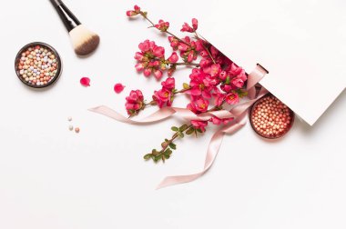 Ball allık rouge ve yüz tozu, makyaj fırçası, açık arka plan üst görünüm düz üzerinde beyaz hediye paketi bahar pembe çiçekler. Farklı makyaj kozmetik. Güzellik moda arka plan alışveriş konsepti