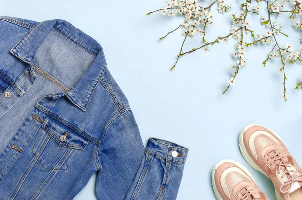 Blauw denim jasje, trendy roze Sneakers, lente bloemen op blauwe achtergrond bovenaanzicht platte lay-out kopiëren. Denim, modieuze jas, vrouwen of mannen trend kleding, Spring Fashion Beauty achtergrond. — Stockfoto