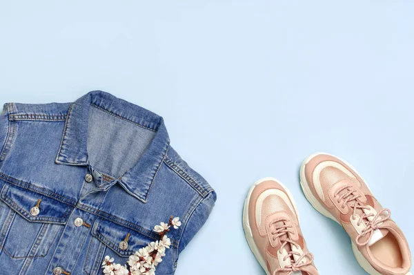 Blauw denim jasje, trendy roze Sneakers, lente bloemen op blauwe achtergrond bovenaanzicht platte lay-out kopiëren. Denim, modieuze jas, vrouwen of mannen trend kleding, Spring Fashion Beauty achtergrond. — Stockfoto