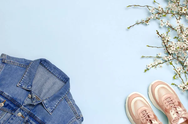 Blå jeansjacka, trendiga rosa sneakers, vårblommor på blå bakgrund översta vyn platt Lay Copy utrymme. Denim, fashionabla jacka, kvinnors eller mäns trend kläder, vårmode skönhet bakgrund. — Stockfoto