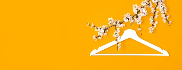 Kreatywne tło urody mody. Biały drewniany wieszak wiszący na wiosennej gałęzi kwitnienia na żółtym tle. Wiosna sprzedaż koncepcja zniżki sklep zakupy pusty wieszak. Płaski widok z góry — Zdjęcie stockowe