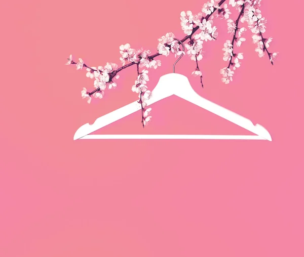 Creative fashion beauty concept. White wooden hanger hanging on the spring flowering branch on pink background. Spring sale concept discount store shopping empty hanger. Flat lay top view copy space.