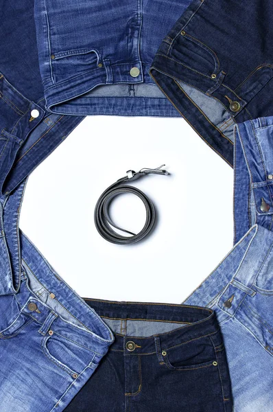Frame of different blue jeans and leather belts isolated on white background top view flat lay. Detail of nice blue jeans. Jeans texture or denim background. Trend clothing. Beauty and fashion