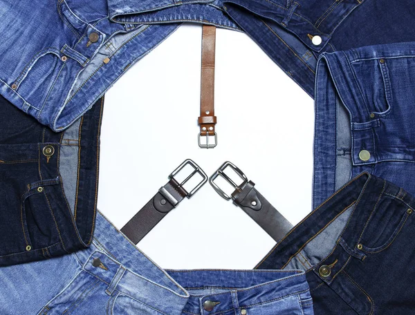 Frame of different blue jeans and leather belts isolated on white background top view flat lay. Detail of nice blue jeans. Jeans texture or denim background. Trend clothing. Beauty and fashion