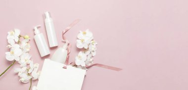 Kozmetik Spa markalama mock-up. Düz üst görünüm Beyaz kozmetik şişe kapları hediye çantası Pembe arka plan üzerinde Beyaz Phalaenopsis orkide çiçekler. Doğal organik güzellik ürün konsepti