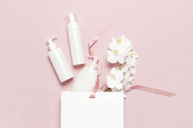 Kozmetik Spa markalama mock-up. Düz üst görünüm Beyaz kozmetik şişe kapları hediye çantası Pembe arka plan üzerinde Beyaz Phalaenopsis orkide çiçekler. Doğal organik güzellik ürün konsepti