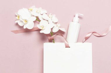 Kozmetik Spa markalama mock-up. Düz üst görünüm Beyaz kozmetik şişe kapları hediye çantası Pembe arka plan üzerinde Beyaz Phalaenopsis orkide çiçekler. Doğal organik güzellik ürün konsepti