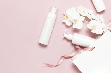 Kozmetik Spa markalama mock-up. Düz üst görünüm Beyaz kozmetik şişe kapları hediye çantası Pembe arka plan üzerinde Beyaz Phalaenopsis orkide çiçekler. Doğal organik güzellik ürün konsepti