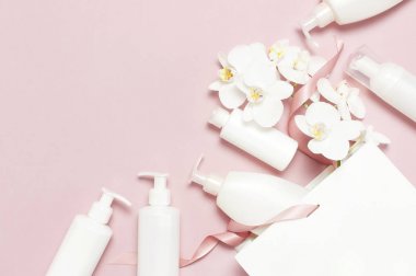 Kozmetik Spa markalama mock-up. Düz üst görünüm Beyaz kozmetik şişe kapları hediye çantası Pembe arka plan üzerinde Beyaz Phalaenopsis orkide çiçekler. Doğal organik güzellik ürün konsepti