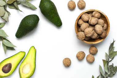 Olgun taze avokado, ahşap kase ceviz, beyaz arka plan üst görünümü düz okaliptüs dalları kopya alanı yatıyordu. Meyve Sağlıklı gıda kavramı, diyet, sağlıklı yaşam tarzı.