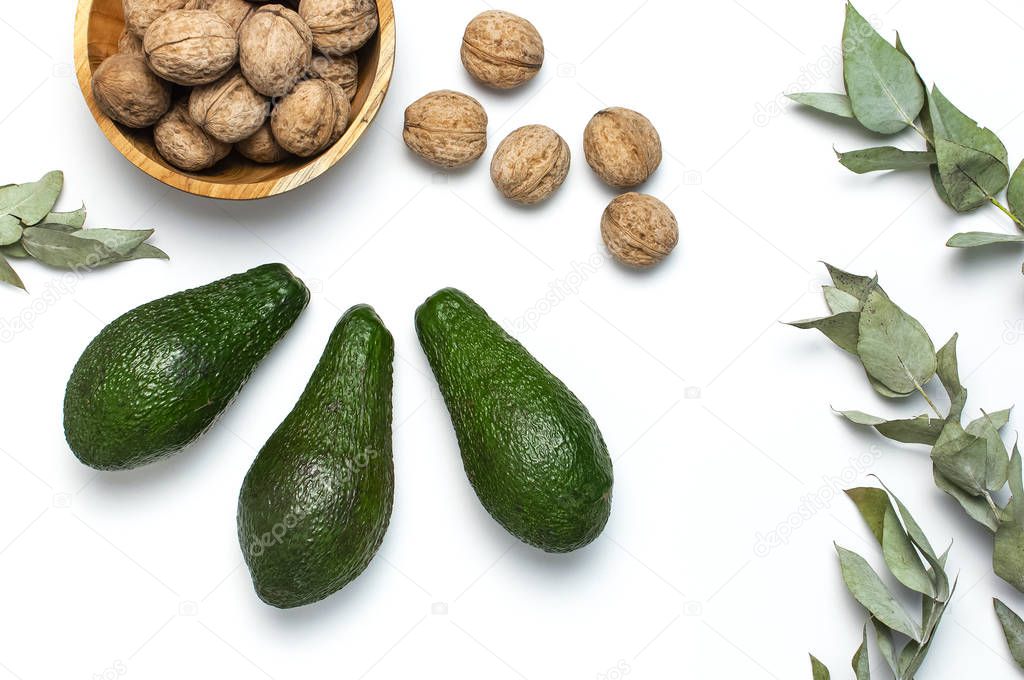 Ripe fresh avocado, walnuts in wooden bowl, eucalyptus twigs on white background top view Flat lay copy space. Fruits Healthy food concept, diet, healthy lifestyle.