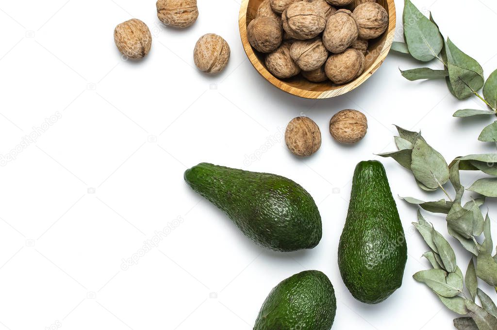 Ripe fresh avocado, walnuts in wooden bowl, eucalyptus twigs on white background top view Flat lay copy space. Fruits Healthy food concept, diet, healthy lifestyle.