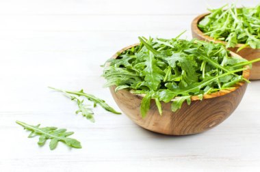 Ahşap kase, rucola salata metin için yer ile beyaz ahşap rustik arka planda üzerinde taze yeşil roka yaprakları. Seçici odak. Roket salata veya roka, sağlıklı gıda, diyet. Beslenme kavramı.