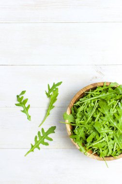 Ahşap kase, rucola salata üzerinde beyaz ahşap rustik arka plan metin için yer ile üstten görünüm üzerinde taze yeşil roka yaprakları. Roket salata veya roka, sağlıklı gıda, diyet. Beslenme kavramı.