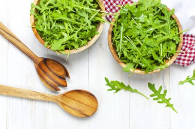 Ahşap kase, rucola salata üzerinde beyaz ahşap rustik arka plan metin için yer ile üstten görünüm üzerinde taze yeşil roka yaprakları. Roket salata veya roka, sağlıklı gıda, diyet. Beslenme kavramı.
