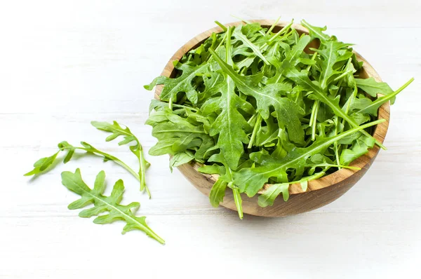 Fresh green arugula leaves on wooden bowl, rucola salad on white wooden rustic background with place for text. Selective focus. Rocket salad or arugula, healthy food, diet. Nutrition concept. — Stock Photo, Image