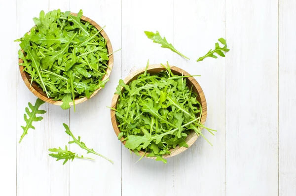 Folhas de arugula verde fresco em tigela de madeira, salada de rucola em branco de madeira rústica vista de fundo superior com lugar para o texto. Salada de foguete ou rúcula, comida saudável, dieta. Conceito de nutrição . — Fotografia de Stock