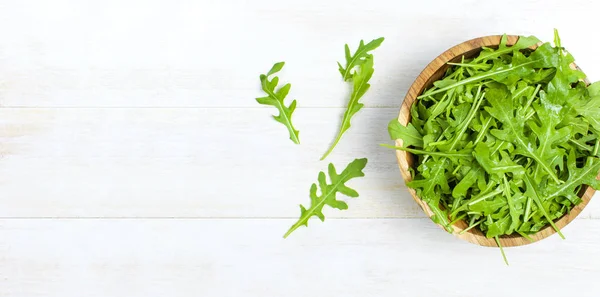 Färska gröna ruccola blad på träskål, rucola sallad på vit trä rustik bakgrund ovanifrån med plats för text. Rucola eller ruccola, hälsosam mat, kost. Nutrition-konceptet. — Stockfoto